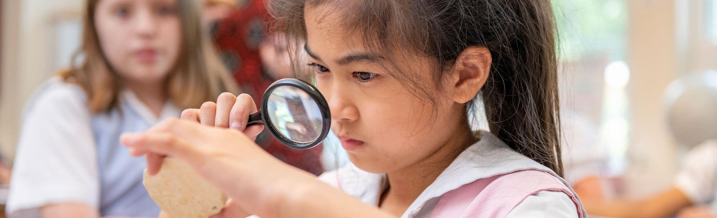 Lower School student in science glass looking through magnifying glass