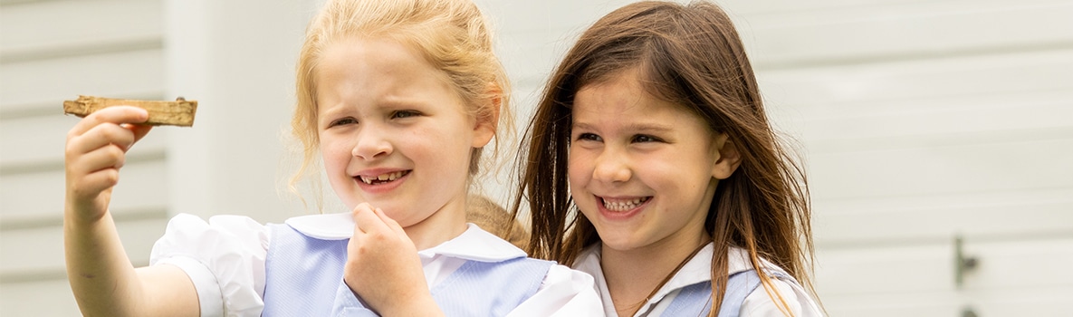 Two students smile while observing insect on a stick.