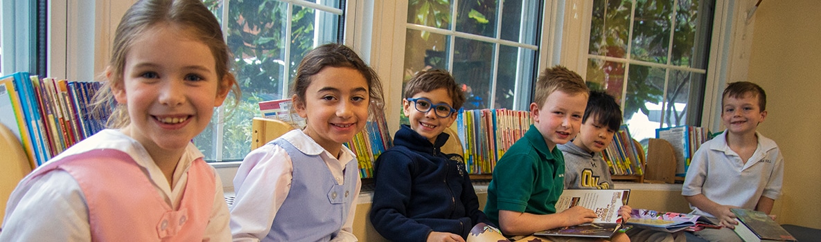 Students in a row smile as they read books in the library.