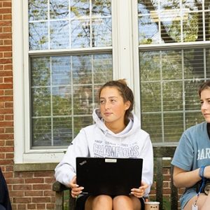 Teacher describes English lesson to three students outside on Connelly Hall porch.